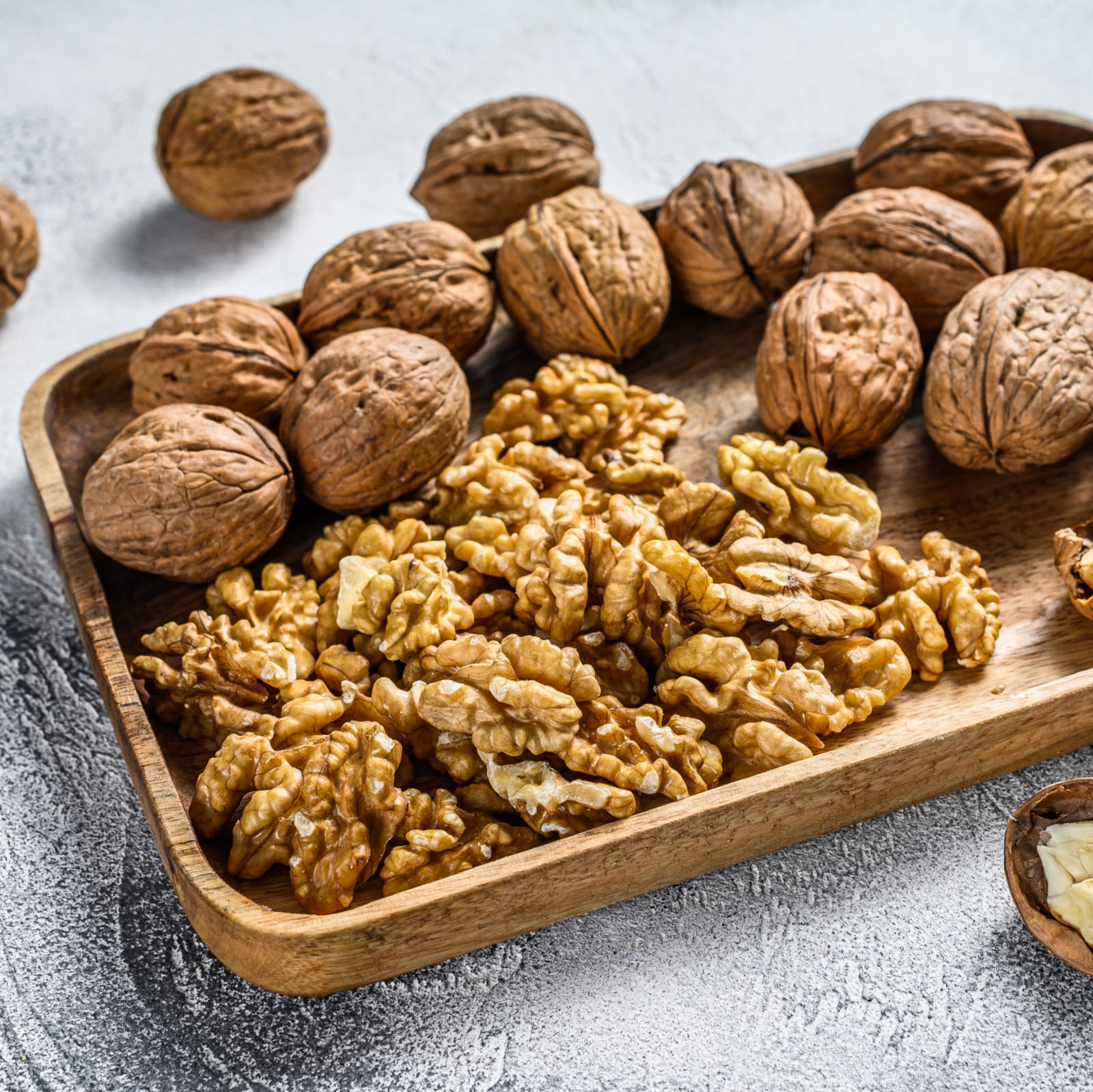 Walnuts in a wooden plate and walnut kernels. Gray background. T